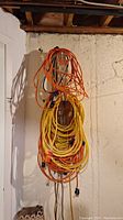Multiple orange and yellow extension cords coiled and hanging on a hook against a basement wall.