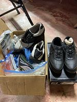 Photo showing three pairs of golf shoes, golf balls in packaging, tees in plastic bags, and folded golf poncho in cardboard box.