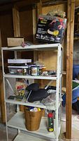 Wide view of metal shelving unit with various hardware items, plastic bins, cans, woven basket, and boxed orbital car waxer on top shelf.