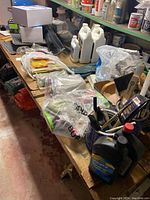Overview of wooden shelving with assorted painting supplies, tools, plastic bags, liquid containers, and plaster materials in basement.