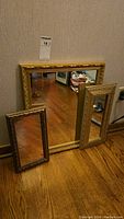 Photo showing the three gilded framed mirrors leaning against a wall on a wooden floor.