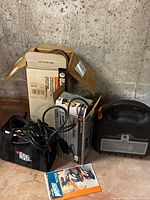 Two Black & Decker sanders along with original box, manual, cords, and accessories on basement floor