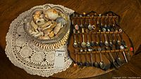 Wide view showing the seashell-filled bowl next to the wooden rack displaying multiple souvenir spoons.