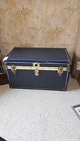 Front closed view of blue metal steamer chest with brass locks and leather handles.