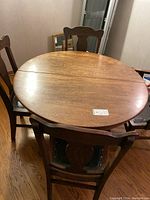 View of round tiger oak table with 3 leaves attached, five leather padded chairs around it.