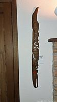 Full view of wooden totem wall carving mounted vertically on wall, showing full height and shape.