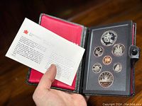 Opened black leather case with red interior showing the 1983 Canadian proof coin set including seven coins and certification leaflet from the Royal Canadian Mint.