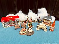 Wide view of the Christmas village set including boxed LEMAX figure, benches, trees, bridge, Santa, and snowy backdrop.