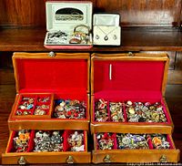 Two wooden jewelry boxes open on a wooden surface showing red velvet interiors filled with assorted jewelry.