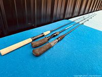 Three fishing poles laid out side by side on a blue surface with diverse handle types, showing overall condition and length.