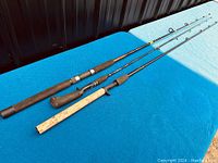Three fishing poles laid out on a blue cloth, showing entire rods with cork and foam handles and metal reel seats