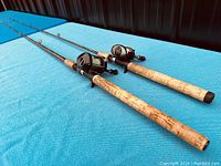 Two vintage fishing rods laid on blue surface, showing cork handles and reels attached.