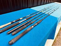 Five fishing rods displayed on blue cloth showing full length