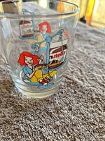Close-up photo of clear glass cup with colorful Nutella-themed cartoon graphics showing a red-haired girl using a scale with Nutella jars.