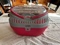 Side view of red and gray plastic rabbit carrying basket with ventilation holes, Living World brand.