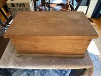 Rectangular wooden dough box on a towel showing top side with natural wood finish and aged patina.