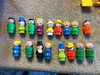 Top view of 15 Fisher Price Little People plastic figures assembled and laid on carpet surface.