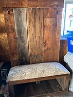 Front view of the hand made wooden coat rack combined with an upholstered bench seat, showcasing rustic wood panels and metal hooks at the top.