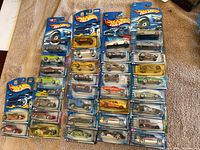 Photo of 34 Hot Wheels cars in original blister packaging arranged on surface. Shows front view of packaging and visible cars inside.