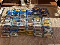Lot of 40 Hot Wheels die-cast toy cars in original sealed packaging laid out in rows on a surface under sunlight.