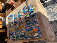 Overview of multiple Hot Wheels blister packs arranged on a towel, displaying variety of cars and a large promotional truck box.