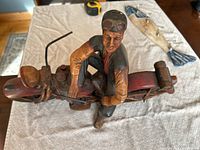 Top view showing man seated on motorcycle sculpture, highlighting the detailed carving and paintwork.