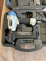 Blue and silver Primatech pneumatic hardwood nailer in black plastic carrying case with nails.