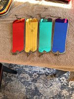 Photo showing four rectangular fishing flashers in red, gold, teal and blue colors laid out on brown towel.