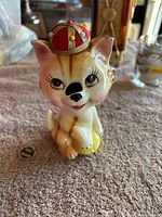 Front view of the ceramic cat figurine showing detailed facial features and the sewing tape measure hat with pins.