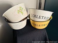 Photo showing four tin enameled bowls stacked: two white with La'Mour Fresh Towels floral design and text, two labeled Toiletries (one yellow, one white with green rim).