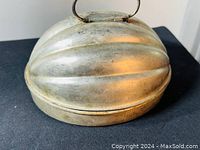 View of the melon-shaped tin pudding mold with a top handle showing ridged surface and patina.