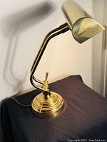 Photo of the full piano desk lamp showing adjustable arm, weighted brass base, and angled shade against a backdrop.