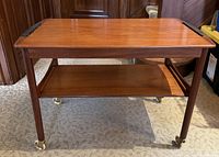 Front facing view of teak two-tier trolley with brass caster wheels
