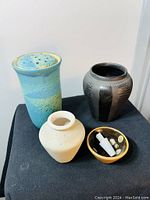 Four ceramic items shown together: turquoise perforated lid vase, beige numbered vase, black patterned vase, small spotted dish with prayer beads.