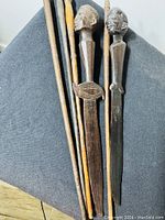 Full view of the lot showing one letter opener and four sticks including two with carved facial heads and two plain sticks.