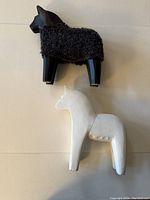 Black and white IKEA DALA horses on a plain background, showing one black horse with wooly coat and one plain white horse