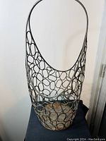 Front view of the rustic large metal basket with artistic openwork oval design and a curved handle at the top, showing rust and patina.