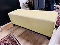 Full view of the lime green velour upholstered rectangular bench with dark wood base on floor, side angled view.