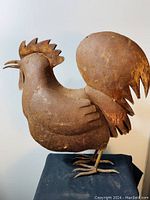 Full side view of the metal rooster sculpture showing length, shape, and support stand.