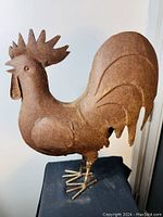 Full view of the vintage metal rooster sculpture showing entire body, legs, and tail, with visible rusting.