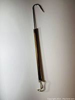 Full length photo showing the fishing gaff hook's wooden handle, metal hook, and attached braided rope loop.