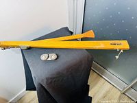 Wooden rudder steering arm with yellow finish on black cloth background, showing full length and paddle end.