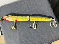 Top view showing the two connected wood segments of the yellow and green painted muskie lure with three treble hooks attached underneath.