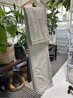 Full view of folded duvet cover and two shams hanging on a wooden hanger among plants