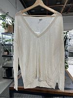 Front view of cream semi-sheer V-neck long sleeve silk knit sweater hanging on wooden hanger.