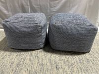 Photo of two grey textured square poofs side-by-side on a carpeted floor, showing front and side.