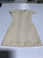 Full front view of the cream wool dress laid flat, showing short sleeves and V-neck shape.