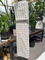 Full view of hanging grey and white striped grey duvet cover and matching pillow sham with several potted plants in the background.