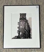 Full view of the framed black and white photograph showing the building and the framing setup on a carpeted floor.