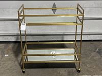 Front view of brass tone metal bar cart showing two mirrored shelves on casters